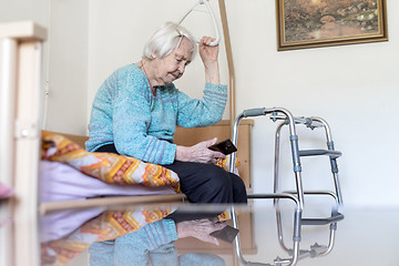 Image showing Elderly 96 years old woman reading phone message while sitting on medical bed supporting her by holder.