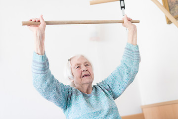 Image showing Elderly 96 years old woman exercising with a stick sitting on her bad.