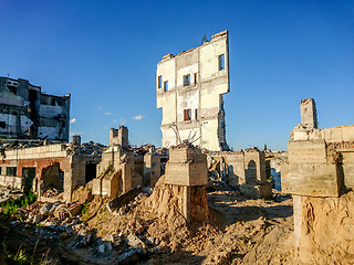 Image showing The ruins of a large destroyed building, pieces of stone, concrete, clay and metal against the blue clear sky.