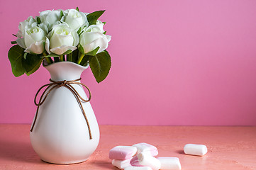 Image showing Copyspace with colorful mini marshmallows on a table next to white roses on a pink background.