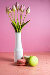 Image showing Makaroons on a pink background next to a bouquet of tulips in a white vase and copy space