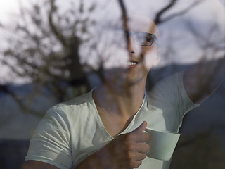 Image showing young man drinking morning coffee by the window