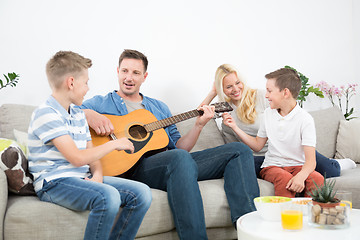 Image showing Happy caucasian family smiling, playing guitar and singing songs together at cosy modern home