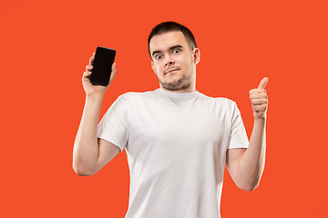 Image showing The happy man showing at empty screen of mobile phone against orange background.