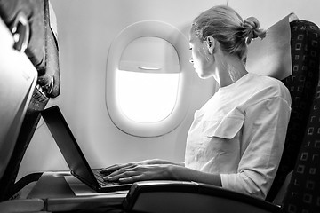 Image showing Attractive caucasian female passenger looking through the plain window while working on modern laptop computer using wireless connection on board of commercial airplane flight