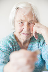 Image showing Sad elderly woman sitting at the table at home and looking miserably at only remaining coin from pension in her hand.