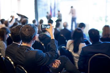 Image showing Businessman takes a picture of corporate business presentation at conference hall using smartphone.