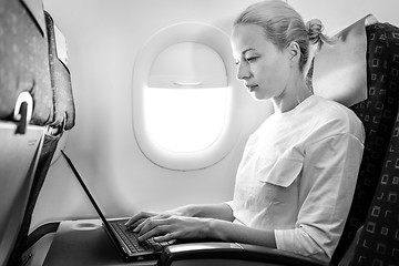 Image showing Attractive caucasian female passenger working at modern laptop computer using wireless connection on board of commercial airplane flight