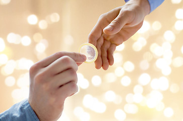 Image showing close up of male gay couple hands giving condom