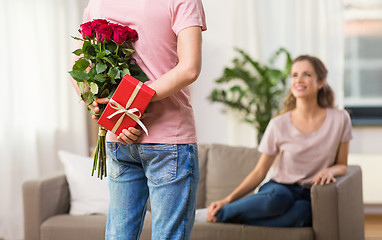 Image showing woman looking at man with flowers and gift at home