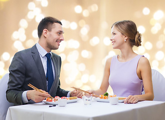 Image showing smiling couple eating sushi rolls at restaurant