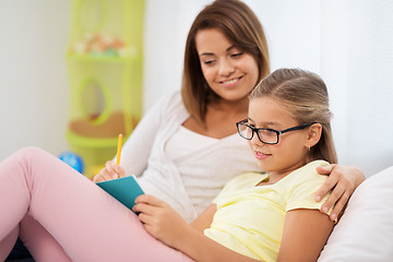 Image showing happy girl with mother writing to notebook at home