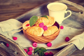 Image showing Croissants with raspberries on a wooden tray. The concept of a wholesome breakfast.