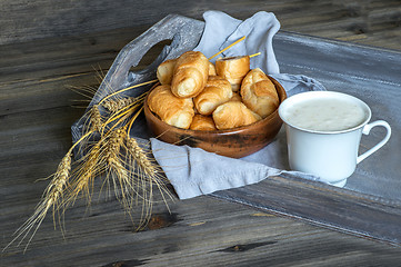 Image showing Croissants, a cup with kefir and ears of grain on a wooden tray. The concept of a wholesome breakfast.