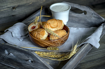 Image showing Croissants, a cup with kefir and ears of grain on a wooden tray. The concept of a wholesome breakfast.