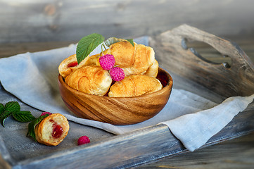 Image showing Croissants with raspberries on a wooden tray. The concept of a wholesome breakfast.