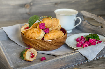 Image showing Croissants with raspberries on a wooden tray. The concept of a wholesome breakfast.