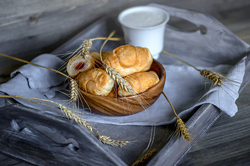 Image showing Croissants, a cup with kefir and ears of grain on a wooden tray. The concept of a wholesome breakfast.