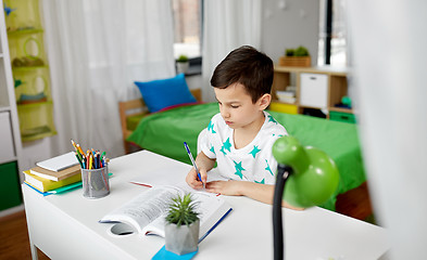 Image showing student boy with book writing to notebook at home