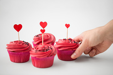 Image showing close up of hand taking cupcakes with heart sticks