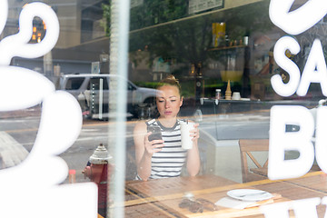 Image showing Thoughtful woman reading news on mobile phone during rest in coffee shop.