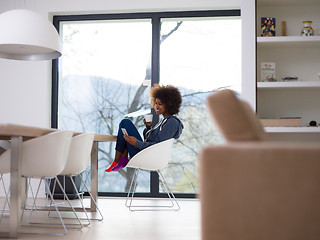 Image showing black woman drinking coffee and using a mobile phone  at home