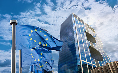 Image showing Blue flag of the European Union with bitcoin icons and a modern building in the form of a symbol of bitcoin against a sky with white clouds