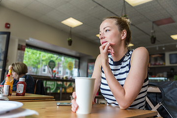 Image showing Young caucasian woman sitting alone in coffee shop thoughtfully leaning on her hand, looking trough the window