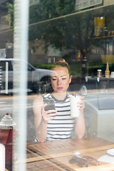 Image showing Thoughtful woman reading news on mobile phone during rest in coffee shop.