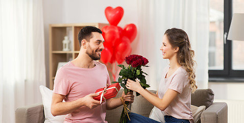 Image showing happy man giving woman flowers and present at home