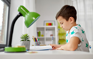 Image showing student boy with book writing to notebook at home