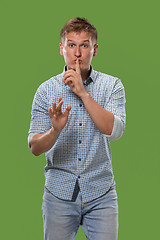 Image showing The young man whispering a secret behind her hand over green background