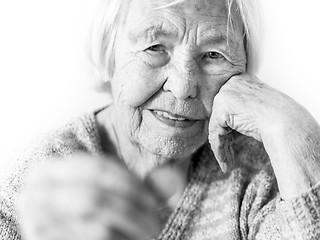 Image showing Cheerful elderly 96 years old woman sitting at table at home happy with a coin in her hand. Saving for retirement and financial planing concept in black and white.