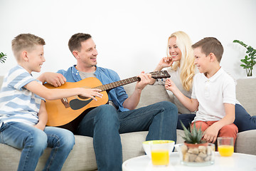 Image showing Happy caucasian family smiling, playing guitar and singing songs together at cosy modern home