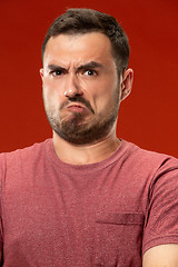 Image showing The young emotional angry man screaming on red studio background