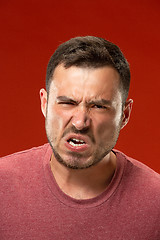 Image showing The young emotional angry man screaming on red studio background