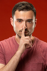 Image showing The young man whispering a secret behind her hand over red background