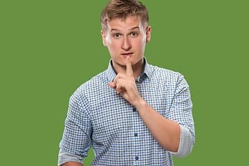 Image showing The young man whispering a secret behind her hand over green background