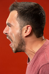 Image showing The young emotional angry man screaming on red studio background