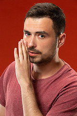 Image showing The young man whispering a secret behind her hand over red background