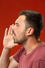 Image showing Isolated on red young casual man shouting at studio