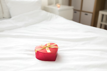 Image showing red gift box in shape of heart on bed at home