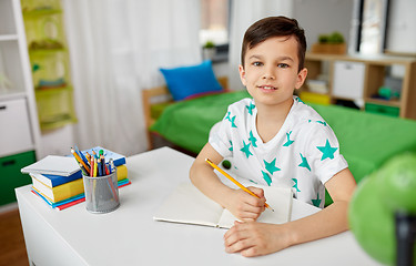 Image showing happy boy writing or drawing to notebook at home