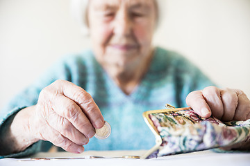 Image showing Concerned elderly woman sitting at the table counting money in her wallet.