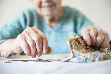 Image showing Detailed closeup photo of unrecognizable elderly womans hands counting remaining coins from pension in her wallet after paying bills.