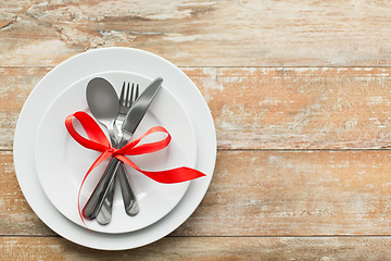 Image showing cutlery tied with red ribbon on set of plates