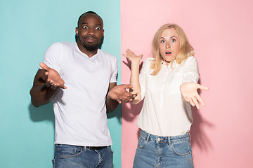 Image showing Closeup portrait of young couple, man, woman. One being excited happy smiling, other serious, concerned, unhappy on pink and blue background. Emotion contrasts