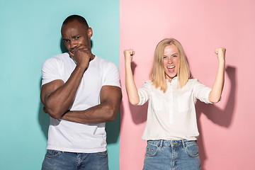 Image showing Closeup portrait of young couple, man, woman. One being excited happy smiling, other serious, concerned, unhappy on pink and blue background. Emotion contrasts