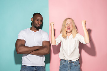 Image showing Closeup portrait of young couple, man, woman. One being excited happy smiling, other serious, concerned, unhappy on pink and blue background. Emotion contrasts