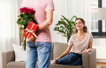 Image showing woman looking at man with flowers and gift at home